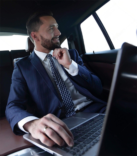 this image shows a smiley face of a businessman in a limousine with his laptop