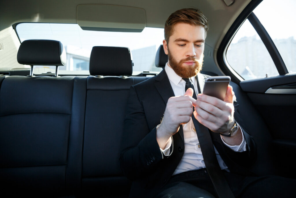 A business man in our classy limo car browsing on his phone with our free wi-fi